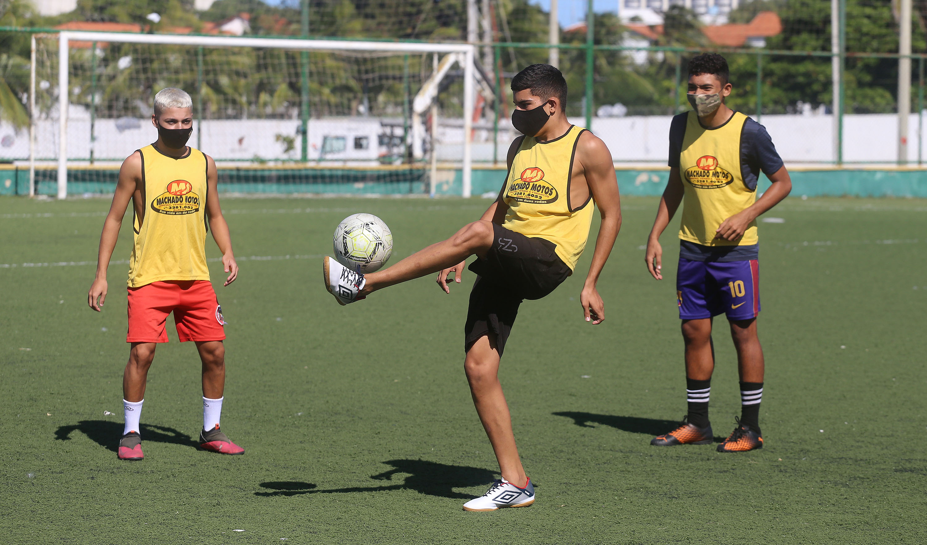 uma rapaz faz uma embaixadinha com uma bola e observado por outros que formam uma roda com ele 